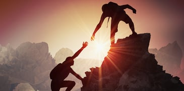 man on top of mountain helping another climber 