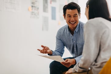 A male bookkeeper in a blue shirt sharing ideas with a prospective female client inside a bright and modern studio