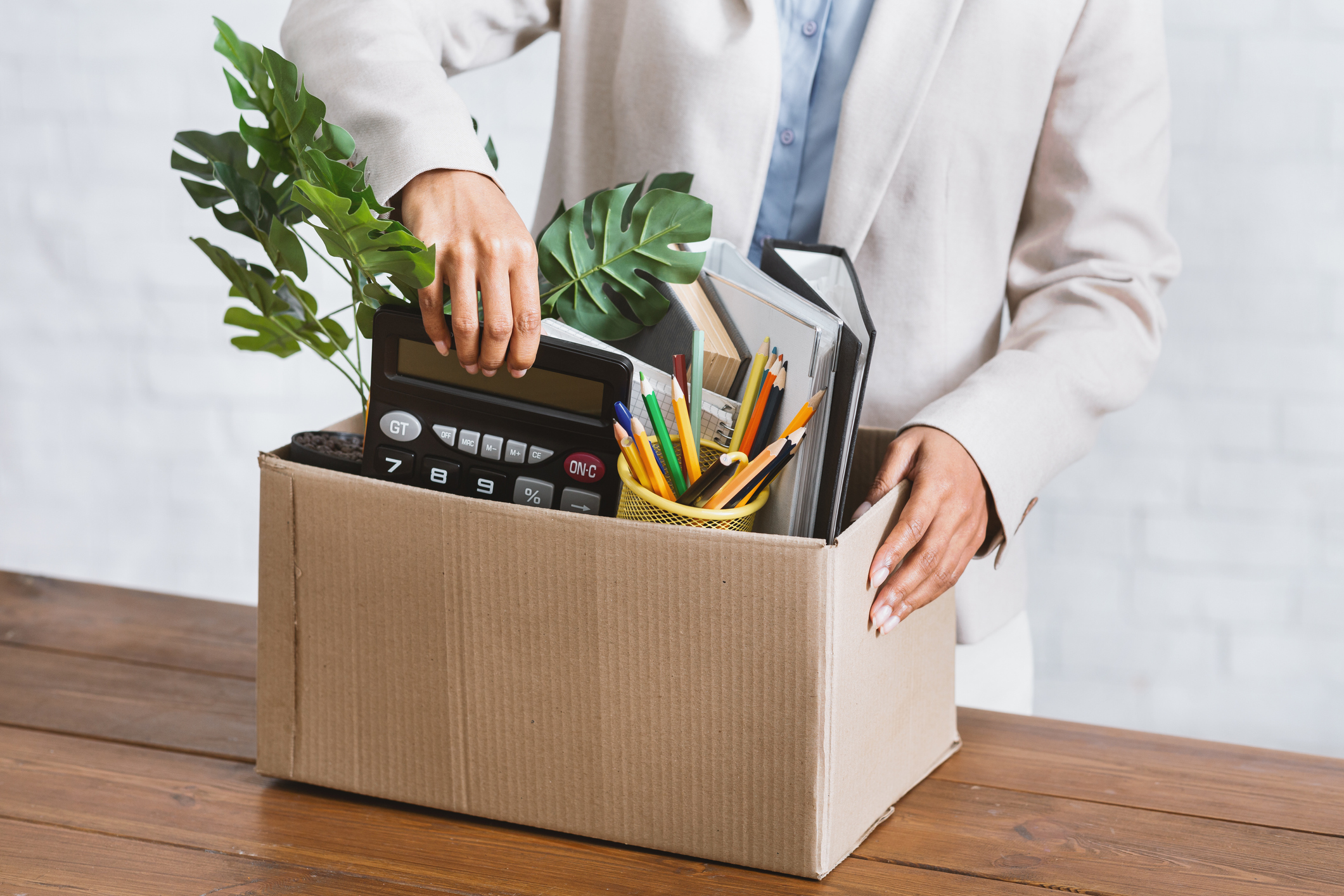 Employee packing a plant, assorted paper, folders, calculator, assorted pens in a box.