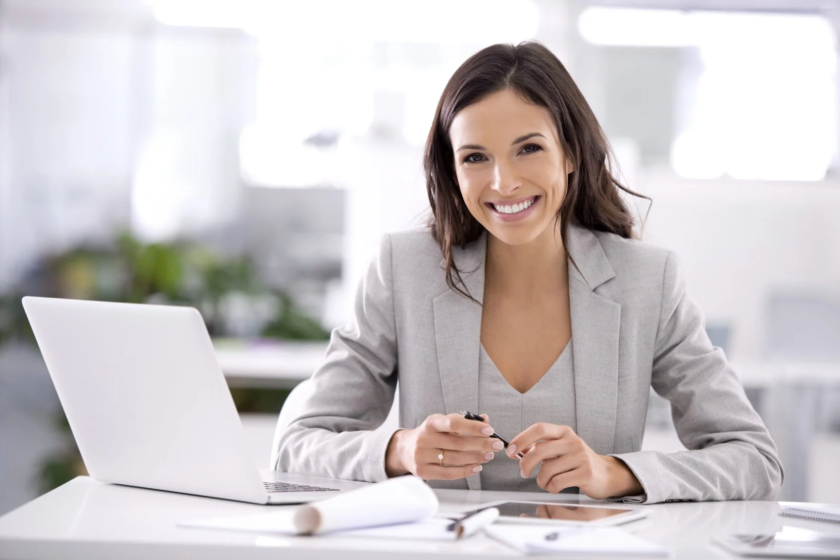 smiling woman holding a pen with laptop on her table